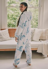 Kapuzen-Einteiler aus weichem, hellblauem Fleece mit einem verspielten Muster von Cartoon-Tieren in dunklerem Blau. Lockere Passform mit Bündchen an Ärmeln und Beinen.