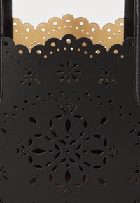 Black leather tote bag with laser-cut floral patterns. Gold scalloped edge features cutouts for added texture and contrast.