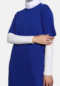 Královsky modré tričko s volným střihem, krátkým rukávem, vyrobené z měkké látky. Přes něj je navlečeno upnuté bílé tričko s dlouhým rukávem.