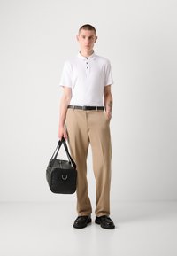 Witte polo shirt met drie knopen, beige broek, zwarte riem, zwarte leren tas met rits en zwarte schoenen. Gladde stofstructuur, nette pasvorm.