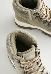 Szare buty trekkingowe z teksturowanym, puszystym kołnierzem, gładką cholewką i trwałą gumową podeszwą. Posiadają beżowe sznurówki i metalowe oczka.