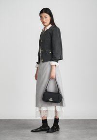 Melna džinsa jaka ar zelta pogām, pelēkas svārki ar mežģīņu apdari, melna rokassomiņa ar logo un melni apavi ar studiem. Redzamas sakrautas tekstūras.