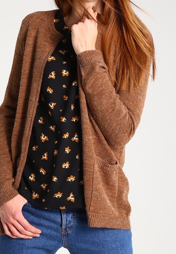 Brązowy dziergany kardigan z otwartym przodem, ściągaczowymi mankietami i dwoma przednimi kieszeniami. Nosi się go na czarnej bluzce z pomarańczowym wzorem lisa. Widać dżinsy.