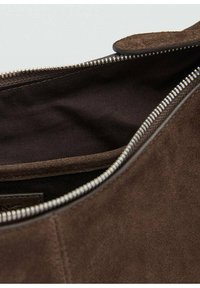 Interior de bolsa de ante marrón, con un forro oscuro y detalles de cremallera plateada. Incluye un pequeño bolsillo en el lateral para almacenamiento adicional.