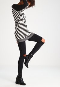 Gestreiftes Langarmhemd in Schwarz und Weiß mit einem grauen Saum, kombiniert mit schwarzen Skinny-Jeans mit Knie-Rissen und schwarzen Stiefeletten.