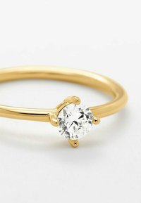 Anello in oro con una pietra preziosa trasparente e rotonda, sostenuta da quattro griffe, con una finitura liscia e lucida e un design slanciato.
