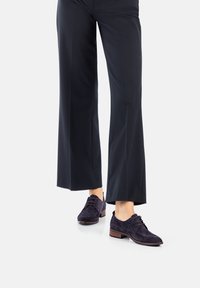 Donkerpaarse suède schoenen met een lage hak, voorzien van vetersluiting en een ronde neus, gecombineerd met brede zwarte broek.