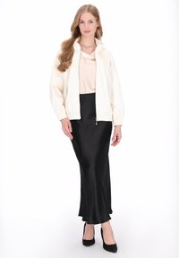 Jachetă albă cu fermoar, manșete elastice, top bej și fustă neagră din satin mulată, completate de pantofi cu toc înalt negri. Texturi netede și design casual.