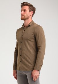 Maglietta a maniche lunghe marrone a coste con colletto button-down, caratterizzata da bottoni frontali e un piccolo logo sul petto.