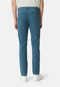 Jasnoniebieskie chinosy mają gładką teksturę, wąski krój i dwie tylne kieszenie. Model nosi białe trampki, co podkreśla casualowy styl.