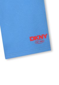 Blauwe stof met rood DKNY-logo en "EST. 1989" gedrukt nabij de zoom, met details van het kledingstuk en de stiksels.