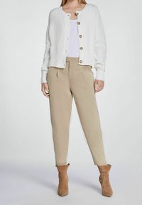 Vit stickad cardigan med knappar, parat med ljusbeige skräddarsydda byxor och bruna ankelstövlar. Slät textur med en avslappnad passform.