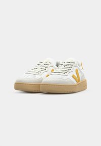 Sneakers in pelle bianca con accenti in suede grigio, loghi laterali gialli, punta perforata e suola in gomma. Presentano lacci piatti e colletto imbottito.