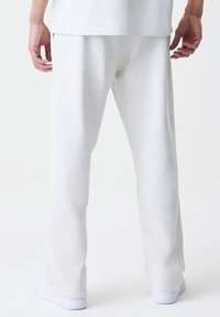 Pantalones de chándal de color gris claro, fabricados con un tejido suave, que presentan un ajuste relajado y un diseño de pierna recta. Cintura elástica y sin bolsillos visibles.
