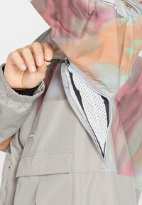 Lichtgewicht beige jack met een kleurrijke, gedessineerde capuchon. Voorzien van een zak met rits en meshvoering en een verstelbare koord bij de hals.