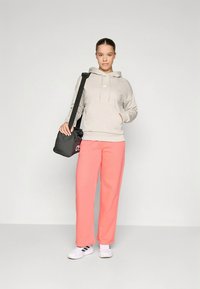 Sweatshirt cinza claro com bolso canguru, combinado com calças de fato de treino coral vivo. Ténis brancos e uma mala preta de ombro completam o visual.