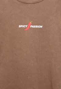 Barna pamut póló kerek nyakkivágással, fehér "SPICY PASSION" felirattal és piros chili paprika grafikával.