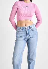 Różowa prążkowana crop top z długimi rękawami i okrągłym dekoltem, w połączeniu z jasnoniebieskimi spodniami typu straight-leg z pięcioma kieszeniami.