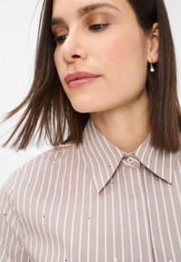 Light beige striped shirt with silver sequins, featuring a classic collar and button closure, smooth texture, and short sleeves.