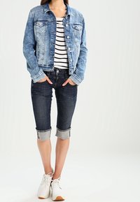 Vaaleansininen farkkutakki, jossa on kulutettu pinta, yhdistettynä tummansinihin lyhytlahkeisiin farkkuihin, joita on käännetty, sekä valkoisiin tennareihin. T-paidan alla on vaakasuorasti raidoitettu malli.