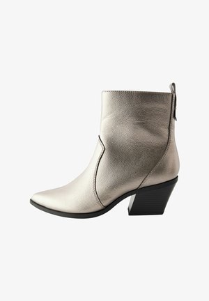 Botín de cuero plateado hasta el tobillo con punta afilada, acabado texturizado y tacón negro apilado. Cuenta con una costura decorativa y un zipper trasero.