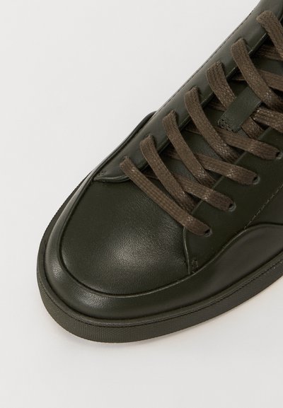 Baskets en cuir vert foncé avec une texture lisse, bout rond et lacets plats marron. La semelle en caoutchouc ajoute du contraste et de la durabilité.