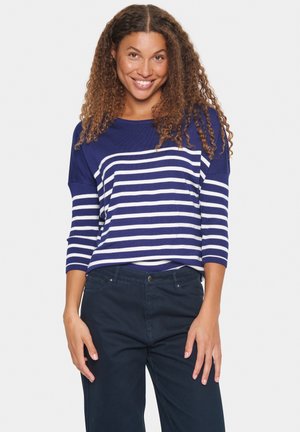 Navyblauer gestreifter Pullover mit weißen Streifen, mit weitem Ausschnitt und Dreiviertelärmeln, kombiniert mit dunklen Hosen.