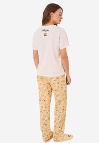 Crème t-shirt met de tekst "Zal jou bedanken" op de achterkant, gecombineerd met gele pyjamabroek met een cartoonpatroon. Gemaakt van zacht katoen.