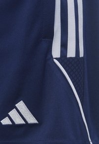 Shorts deportivos color marino con diseño de tres franjas blancas, que cuentan con un bolsillo texturizado y un prominente logo blanco de Adidas. Textura de tejido suave.