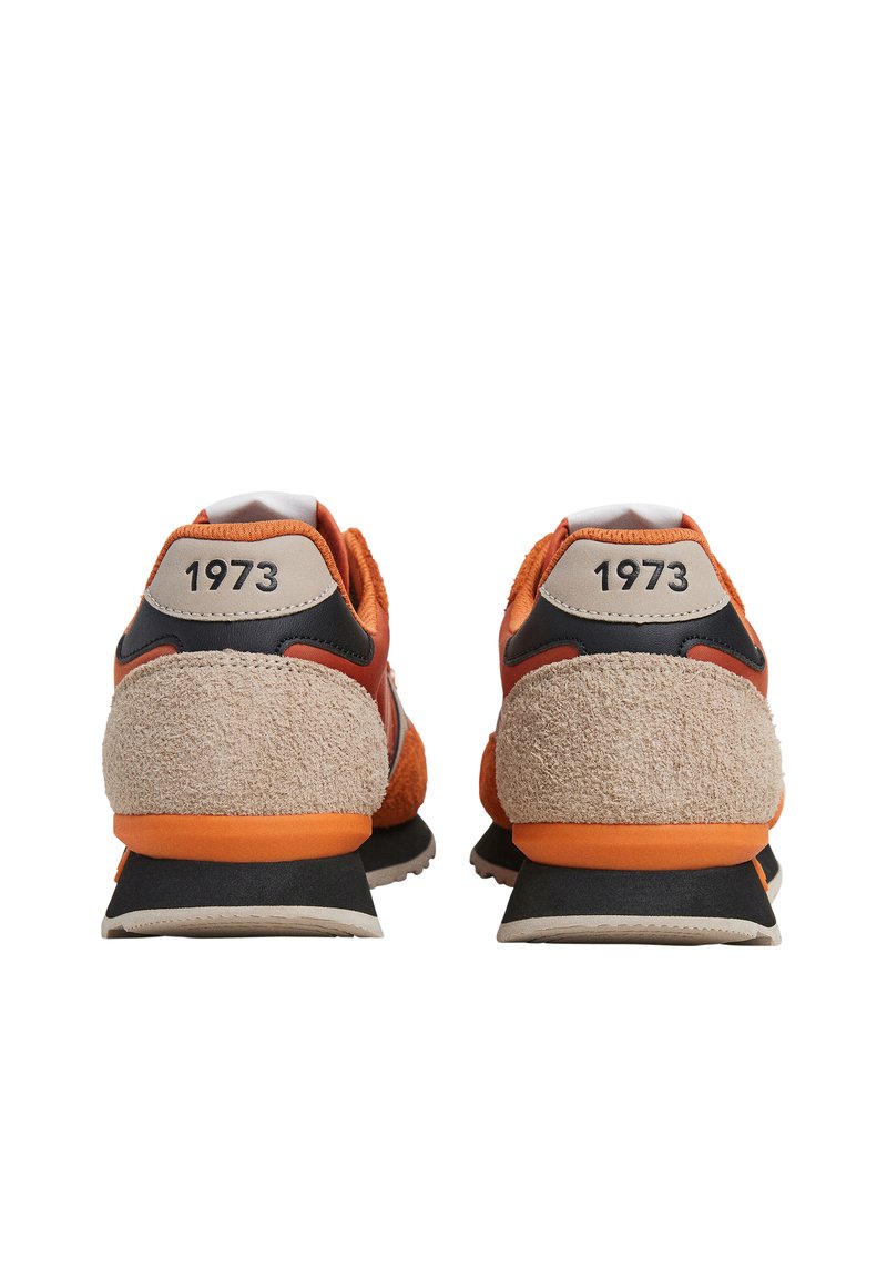 Par de zapatillas deportivas naranjas y beige mostradas desde atrás, con tacones de ante texturizado y "1973" impreso en las lengüetas del talón.