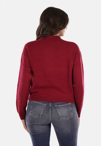 Maglione rosso a maglia con collo alto, polsini e orlo a coste, e una vestibilità comoda, abbinato a jeans blu attillati.
