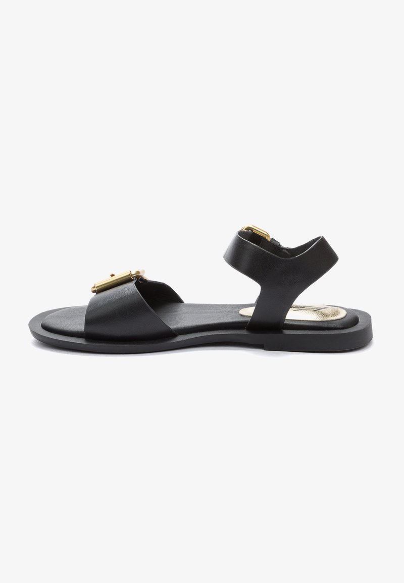 Sandalia de piel negra con accesorios dorados, diseño de punta abierta, dos correas anchas y una plantilla texturizada. Suela plana con un perfil minimalista.