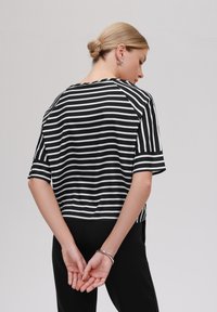 Black and white striped short-sleeve top with a relaxed fit and raglan sleeves, paired with black pants. Simple silver bracelet on wrist.
