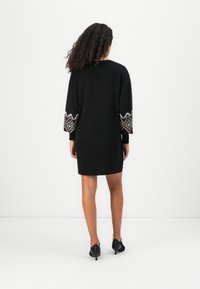 Zwarte jurk met driekwartmouwen, voorzien van kleurrijke geborduurde patronen op de boorden en een ontspannen silhouet. Glad textuur.
