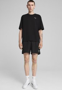 Černé tričko Puma s krátkým rukávem, spárované s černými cargo šortkami s kapsami, a bílými ponožkami a botami Puma. Jednoduchý design.