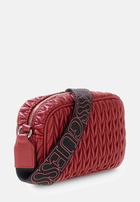 Czerwona pikowana skórzana torebka na ramię z złotym zamkiem i czarnym paskiem, z wyrazistym czerwonym napisem marki.