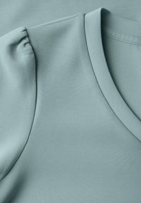 Nahaufnahme eines hellblauen Stoffes, der eine glatte Textur, einen V-Ausschnitt und detailreiche, geraffte Puffärmel präsentiert und das Design sowie die Nähte hervorhebt.