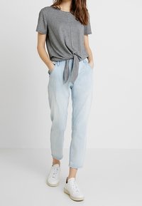 Černobílý kostkovaný tričko s uzlem v přední části, v kombinaci se světle modrými, volnými džíny a bílými teniskami. Hladký povrch tkaniny.