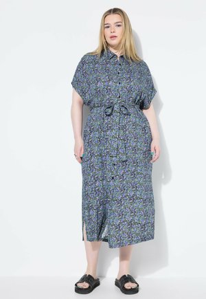 Vestido maxi floral en tela azul, verde y morado. Con botones, mangas cortas, cintura ceñida y aberturas laterales. Sandalias de plataforma negras.