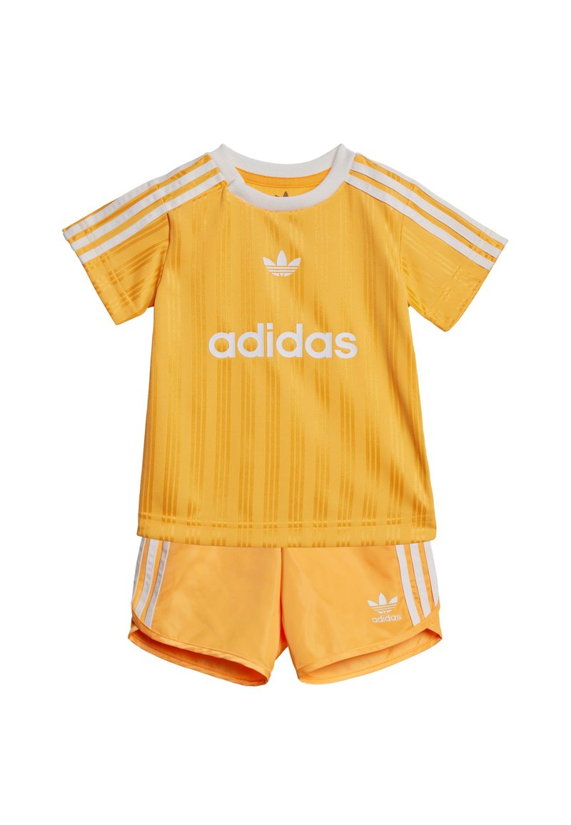 Completo sportivo Adidas giallo composto da una maglietta a maniche corte con righe verticali e logo bianco, abbinata a pantaloncini coordinati con tre righe bianche.