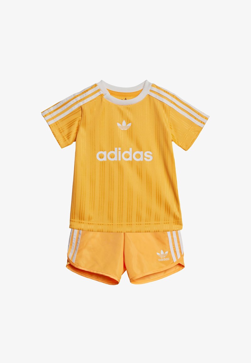 Completo sportivo Adidas giallo composto da una maglietta a maniche corte con righe verticali e logo bianco, abbinata a pantaloncini coordinati con tre righe bianche.