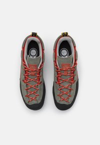 Scarpe da trekking in suede grigio con suole in gomma nera, lacci rossi e colletto imbottito. Caratterizzate da logo e linguette sul tallone.