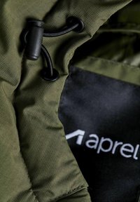Olivengrøn jakke stof med en glat tekstur, som har en sort snøre med toggle og et sort mærke med hvidt logodetalje.