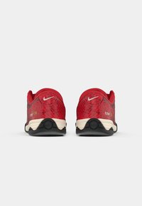 Par de sapatilhas vermelhas da Nike com solas pretas e brancas, vistas por trás, apresentando um padrão texturizado e pequenos logótipos brancos nos calcanhares.