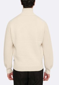 Crèmefarbener gestrickter Pullover mit hohem Kragen, gerippten Bündchen und Saum, ausgestattet mit einer strukturierten Rückseite und seitlichen Details.