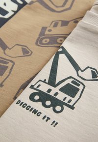 To stk. T-shirts i stof: én i tan med et gravemaskine mønster, én i creme med en stor grøn gravemaskine grafik og teksten "DIGGING IT !!".