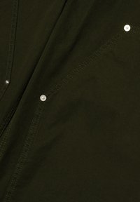 Olivengrüner Stoff mit glatter Textur, diagonal gesteppt und mit silbernen Druckknöpfen. Einfaches Design mit minimaler Gestaltung.