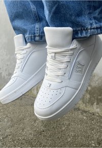 Hvite lær høyt opp sneakers har en polstret krage, perforert tåboks, flate snører og teksturerte sidepaneler for ekstra detaljer.