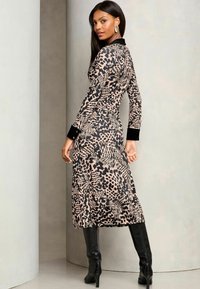 Abito animalier beige e nero, a maniche lunghe con colletto e polsini neri. Indossato con stivali neri fino al ginocchio, in tessuto testurizzato.