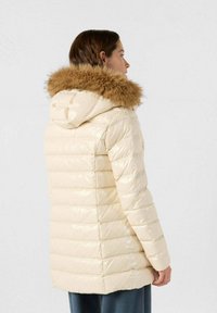 Chaqueta acolchada crema con capucha de piel marrón desmontable, diseño acolchado, acabado brillante y bolsillos laterales, vista desde la parte posterior.